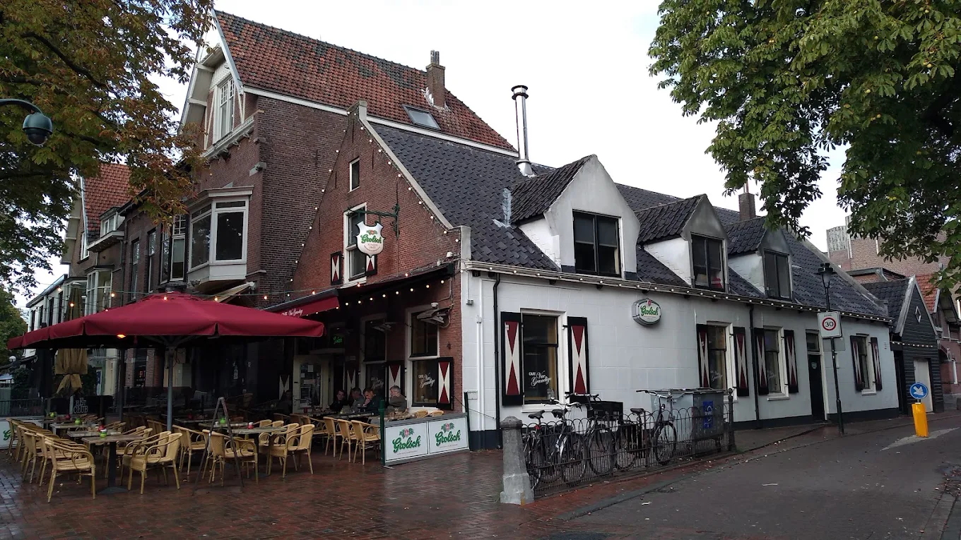 Het terras voor het café, met rode parasol en rieten stoelen op de stoep